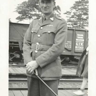 Black and white photograph. Archie poses and smiles for the camera in his uniform, in front of a train car.