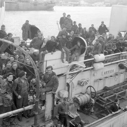 Black and white photograph. The top deck of a ship is crowded with men, sitting and standing on every available surface.