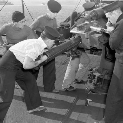 Black and white photograph. Three sailors work to fire a large gun.