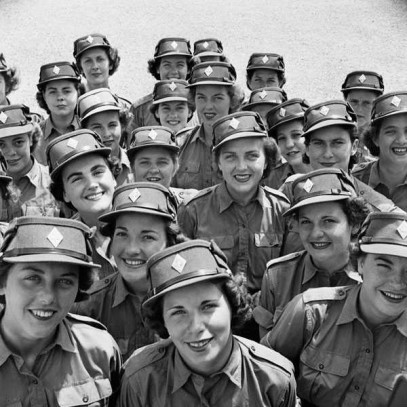 Black and white photograph. A large number of women smile up at the camera. Their faces are clearly visible, and they all wear the khaki cap of the Canadian Women's Army Corps.