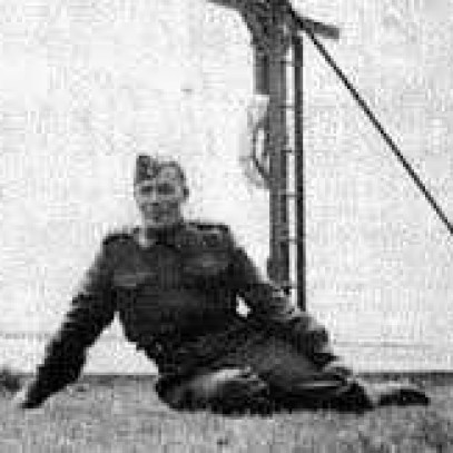 Black and white photograph. Joseph Dreaver, in uniform, sits with his legs curled under him, leaning on his right hand. He looks relaxed.