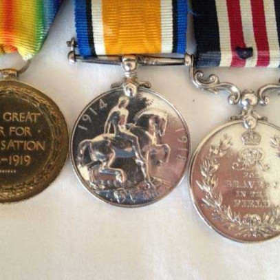 Colour photograph of three First World War medals: Victory Medal (rainbow ribbon, circular, gold);  British war medal (blue/black/white/orange striped ribbon, circular, silver); Military Medal (navy/white/red striped ribbon, circular, silver).