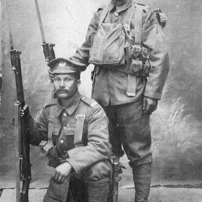 Black and white photograph. Two men in full Canadian Expeditionary Force uniforms and kit pose for a photo. One (Mitsui) stands, while the other (Shishido) kneels. Both hold rifles with bayonets attached.