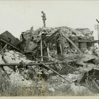 Black and white photograph. A lone soldier stands on the ruins of a sugar factory. Various mechanical implements are visible in the rubble.