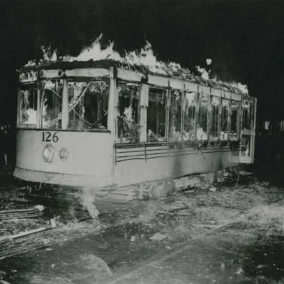 Black and white photograph. A tram car burns in the dark.