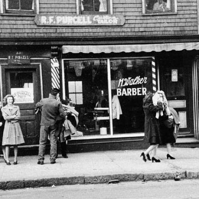 Black and white photograph. Men and women walk by trashed storefronts with arms full of merchandise.
