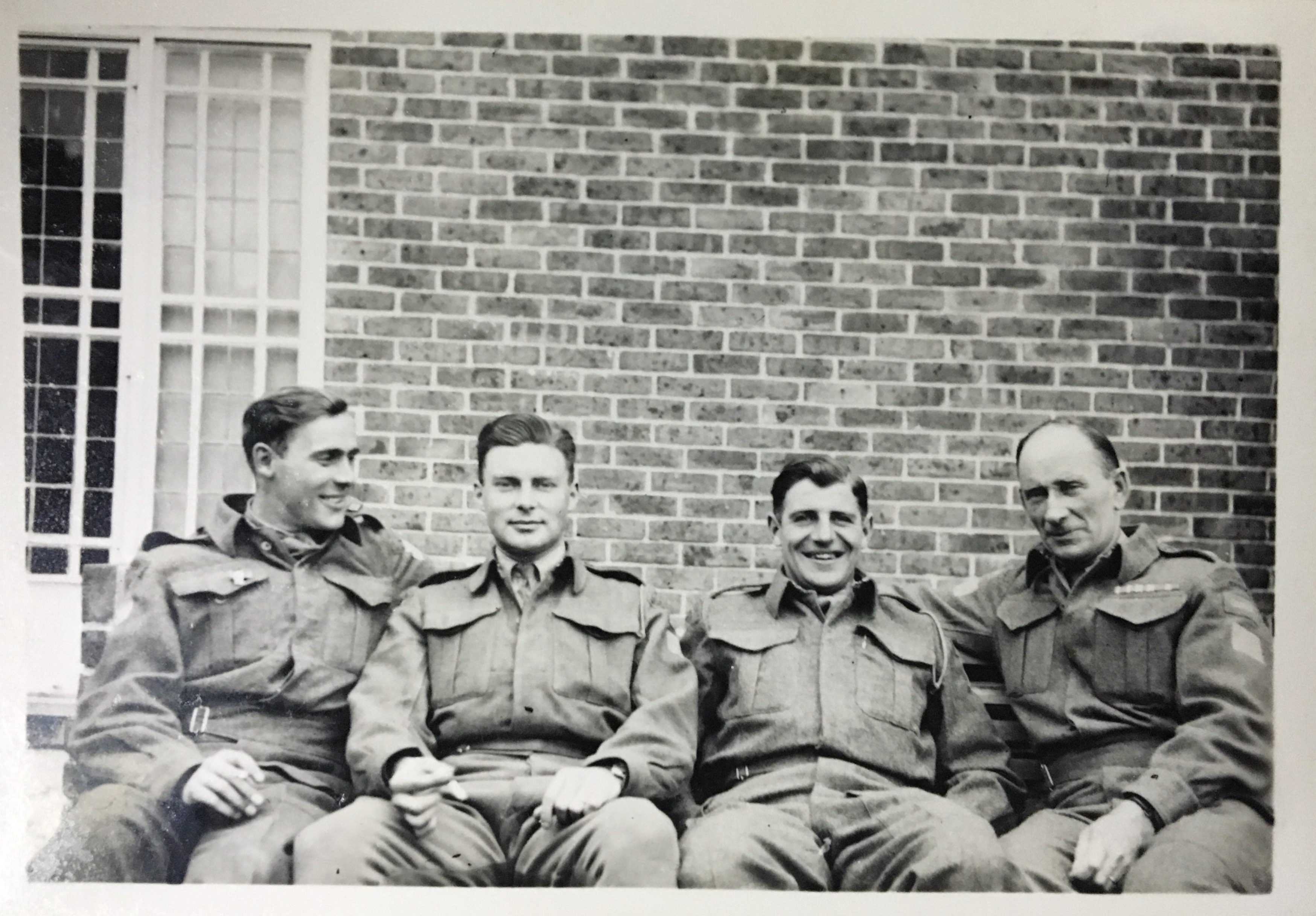 Black and white photograph. Archie, far right, sits on a bench with three much younger men. All are in uniform and are smiling.