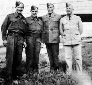 Black and white photograph. Four men in uniform stand in a row, smiling at the camera.
