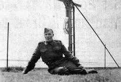 Black and white photograph. Joseph Dreaver, in uniform, sits with his legs curled under him, leaning on his right hand. He looks relaxed.