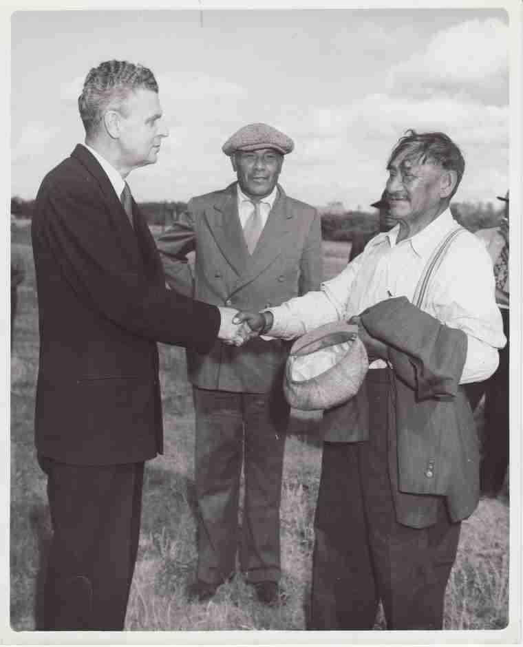 Black and white photograph. John Diefenbaker (left) shakes hands with a labourer. Joseph Dreaver stands behind them in centre.