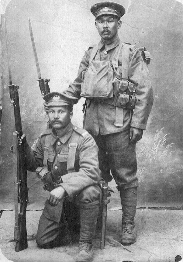 Black and white photograph. Two men in full Canadian Expeditionary Force uniforms and kit pose for a photo. One (Mitsui) stands, while the other (Shishido) kneels. Both hold rifles with bayonets attached.