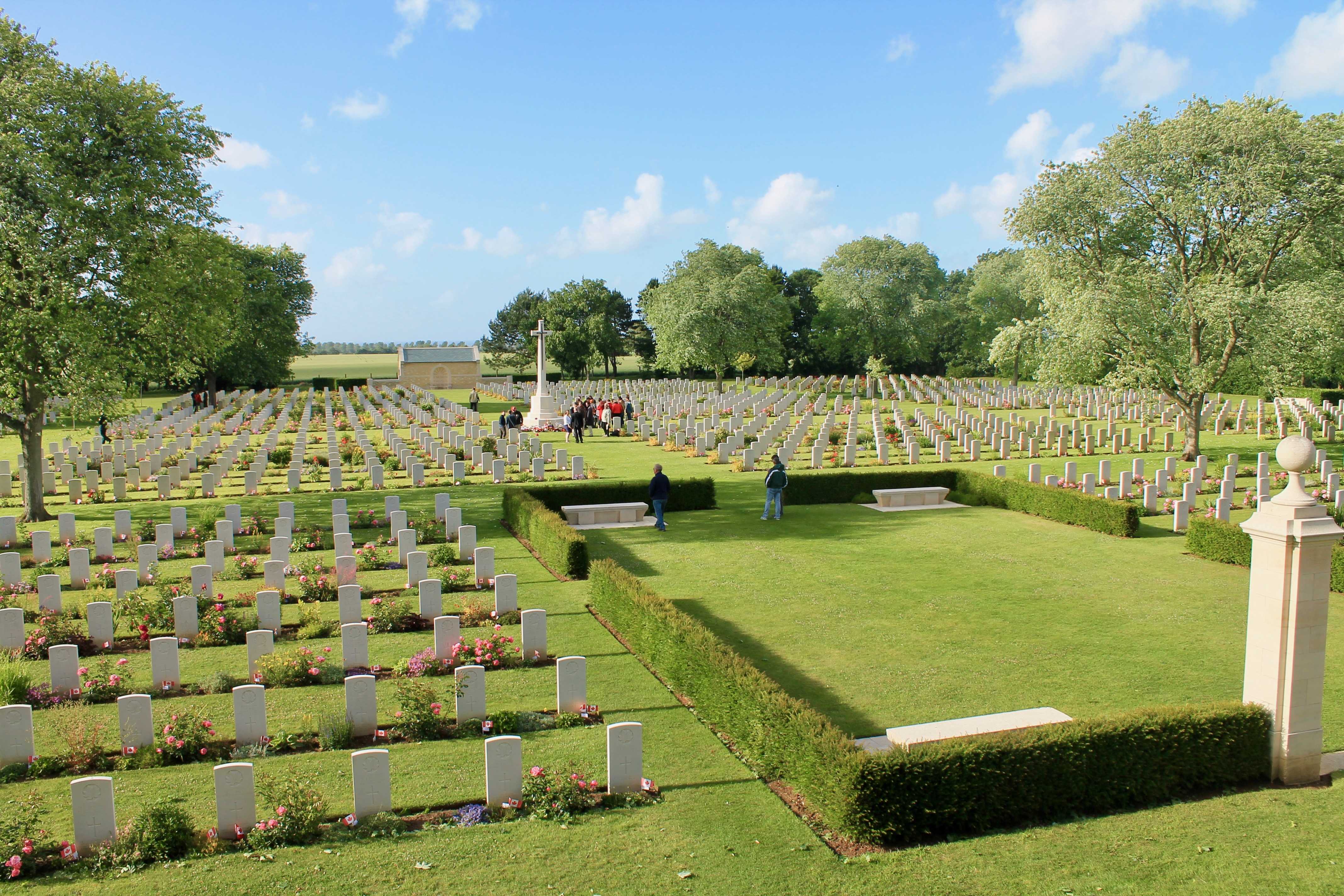 Colour photograph. A view of a military cemetery, with uniform white gravestones in neat rows.