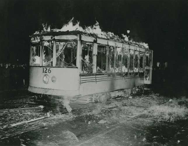 Black and white photograph. A tram car burns in the dark.