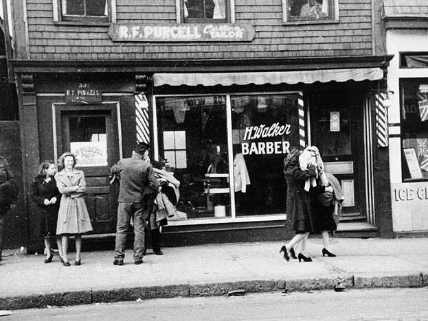 Black and white photograph. Men and women walk by trashed storefronts with arms full of merchandise.